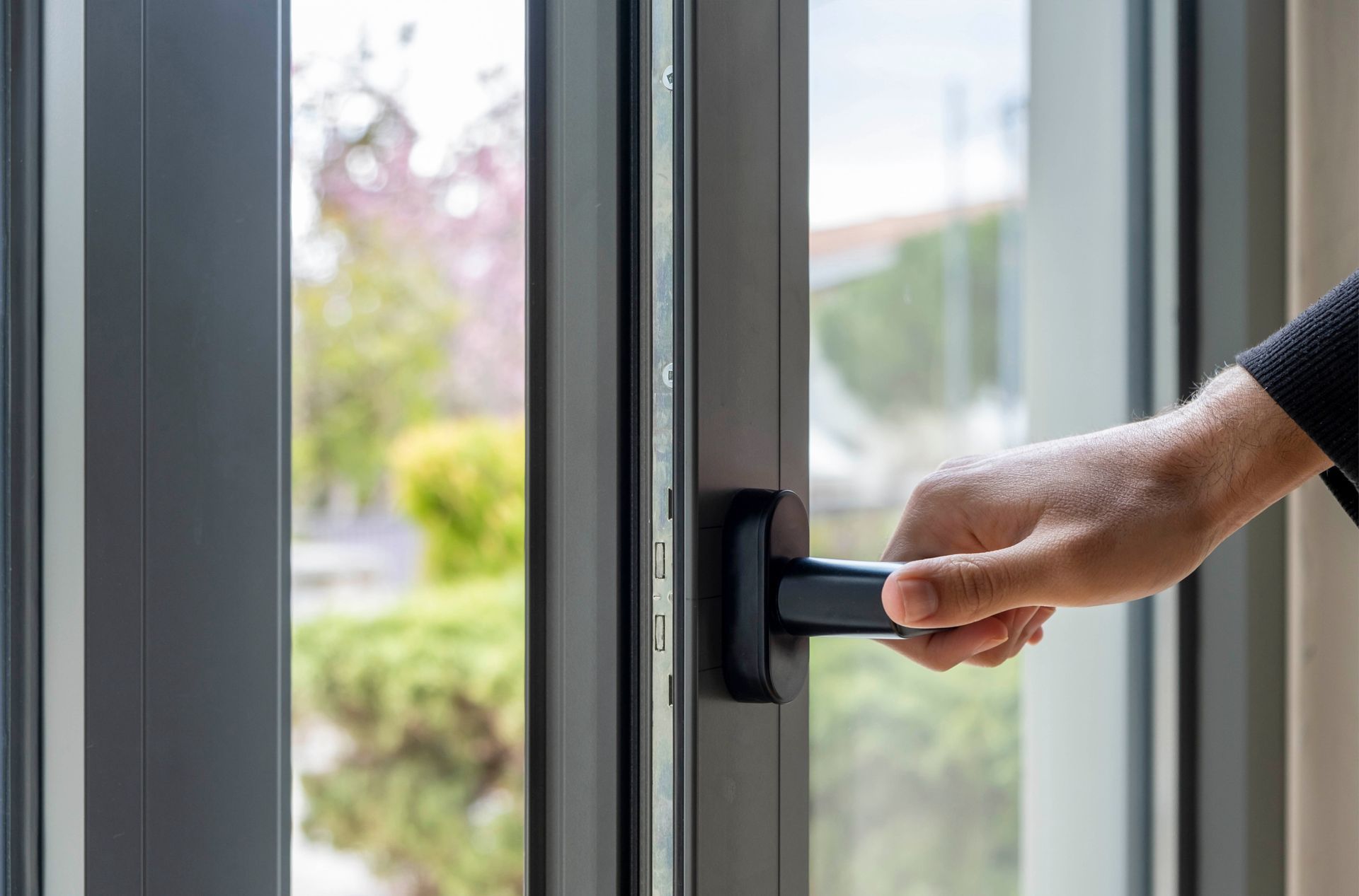 Eine Person öffnet ein Fenster mit einem schwarzen Griff.