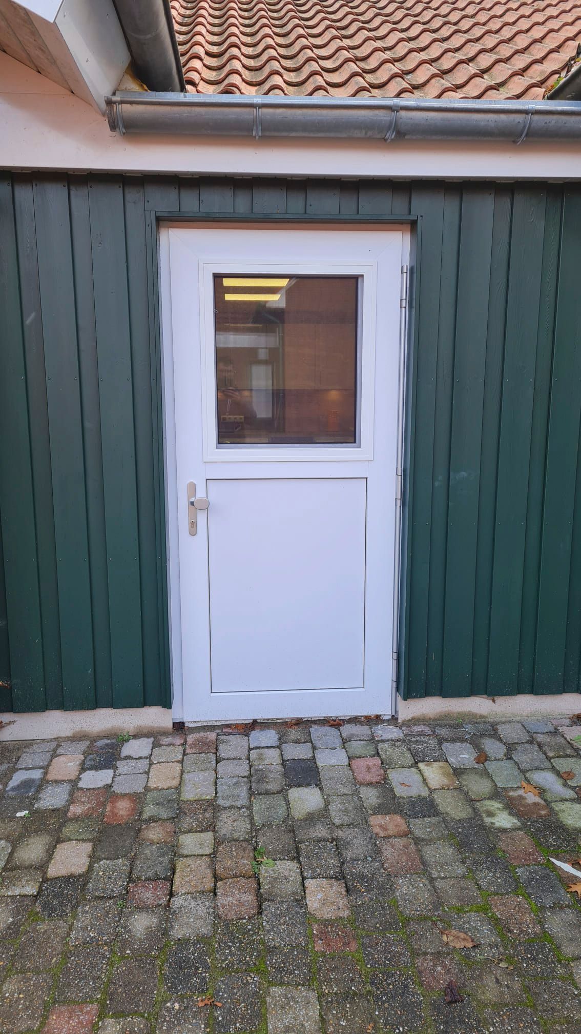 An der Seite eines grünen Gebäudes befindet sich eine weiße Tür.