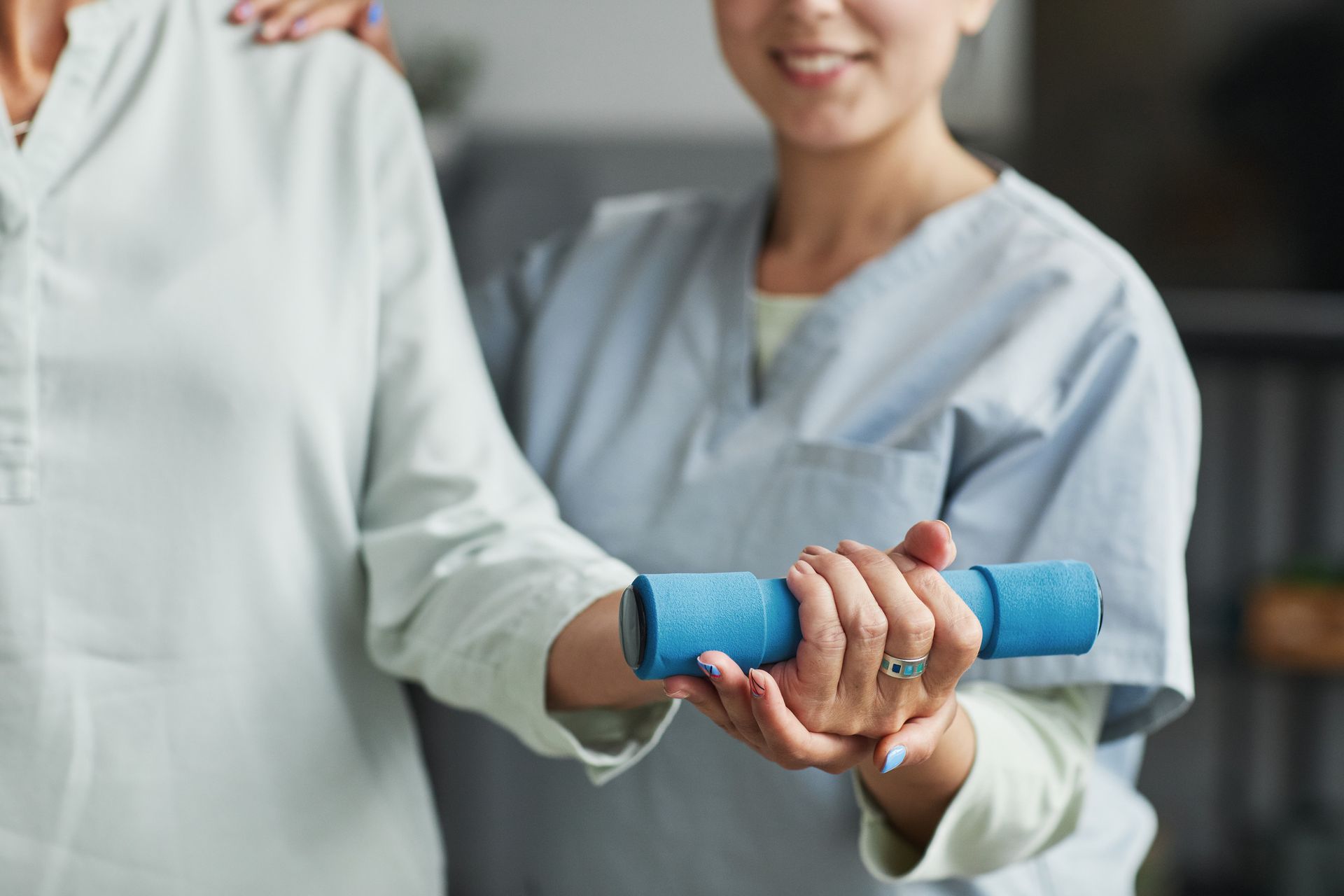 Cuidador ayudando a una persona mayor con ejercicios de brazos, sosteniendo una mancuerna azul en el interior.