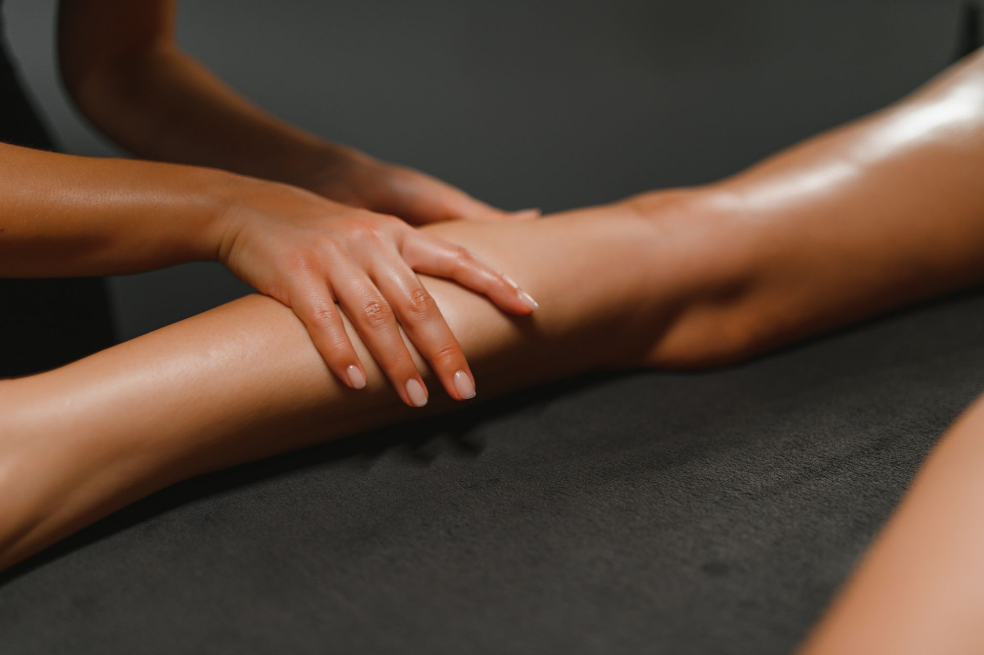 Manos masajeando una pierna, sobre una superficie oscura, posiblemente en un entorno de spa.