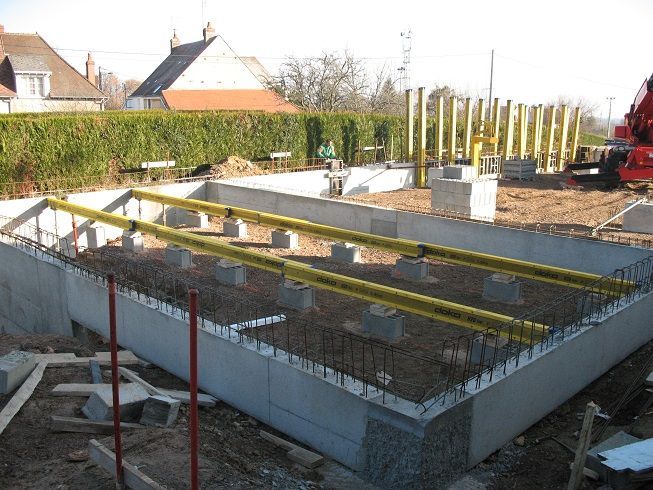 Fondations de maison en construction avec murs en béton, armatures et coffrage en bois sur un site ensoleillé