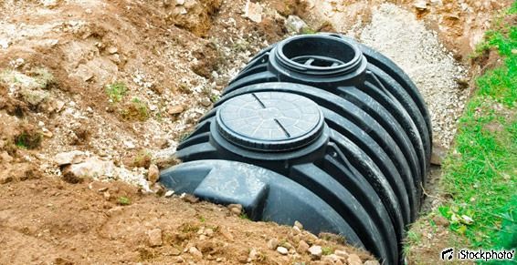 Fosse septique en plastique noir enterrée dans une tranchée de terre à côté de l'herbe verte.