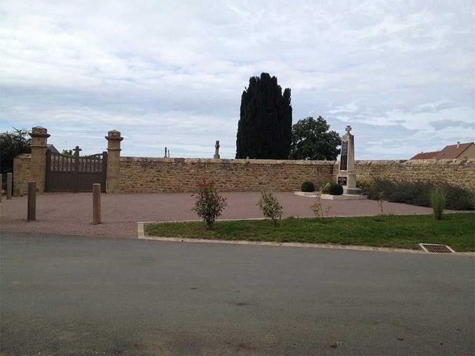 Vue tranquille d'un cimetière, avec un mur de pierre et un portail, sous un ciel nuageux.