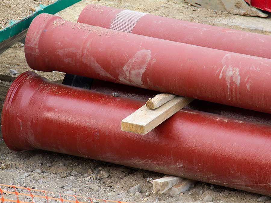 Des tuyaux rouges empilés à l'extérieur sur du gravier, avec un bloc de bois entre eux