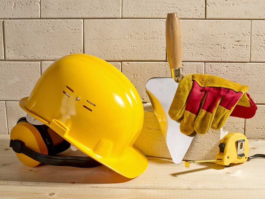Casque jaune, gants de travail, truelle et mètre ruban sur une surface en bois contre un mur de briques