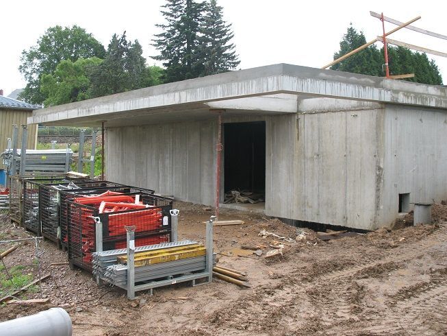 Bâtiment en béton en construction, matériaux empilés et sol boueux à l'extérieur