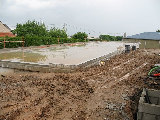 Dalle de fondation en béton inondée sur un chantier boueux sous un ciel couvert