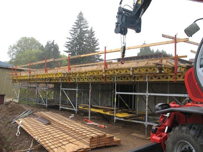 Échafaudages de chantier à côté d'un site boueux, avec une grue soulevant des matériaux au-dessus d'une plateforme de coffrage en béton.