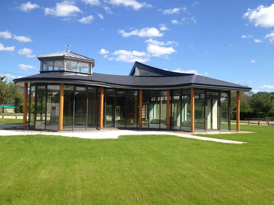 Pavillon moderne en verre avec un toit sombre dans un champ verdoyant sous un ciel bleu