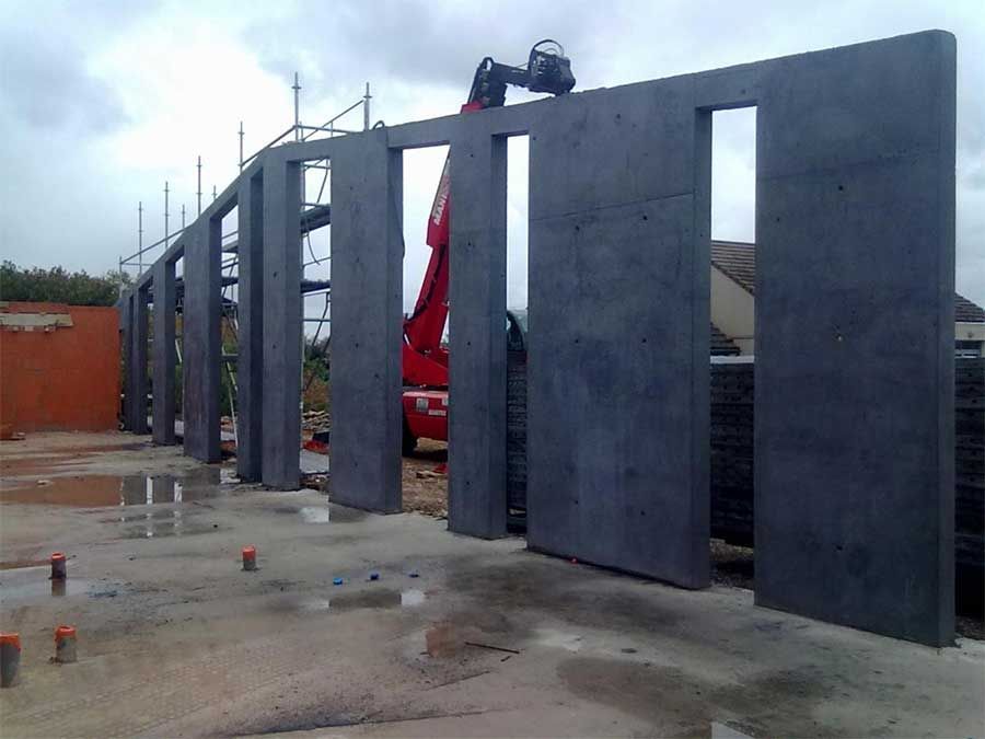 Des panneaux muraux en métal sombre sont installés sur un chantier de construction, avec une grue rouge visible derrière eux.