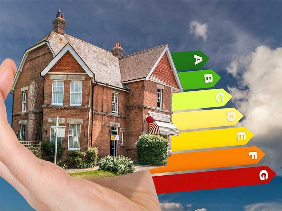Main tenant une maison en briques avec des barres colorées indiquant l'efficacité énergétique, allant du vert A au rouge G.
