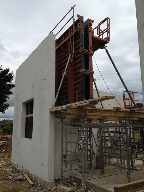 Maison en béton blanc partiellement construite, avec échafaudages et coffrages de chantier à l'extérieur.