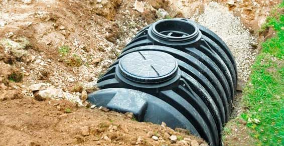 Fosse septique en plastique noir nervuré, enterrée dans une tranchée de terre à côté de l'herbe verte.