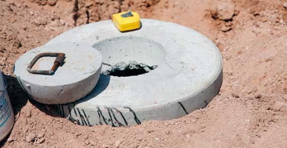 Plaque d'égout en béton posée sur de la terre, avec un petit outil jaune posé dessus.