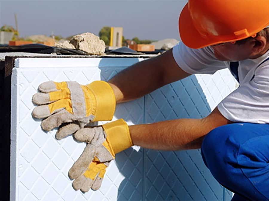 Ouvrier portant un casque orange applique des panneaux isolants sur un mur extérieur
