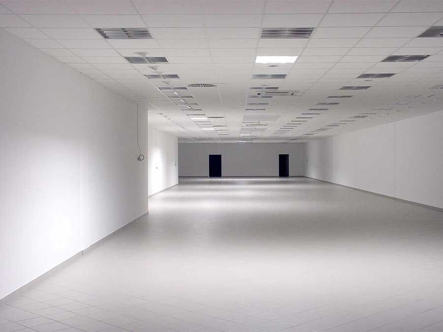 Bureau blanc vide avec plafond carrelé, sol gris et portes noires au loin