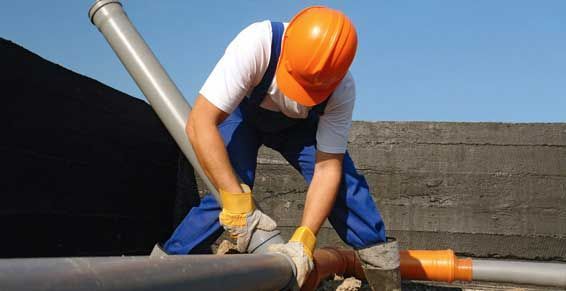 Ouvrier portant un casque et des gants orange installant de l'isolant sur une canalisation de toit
