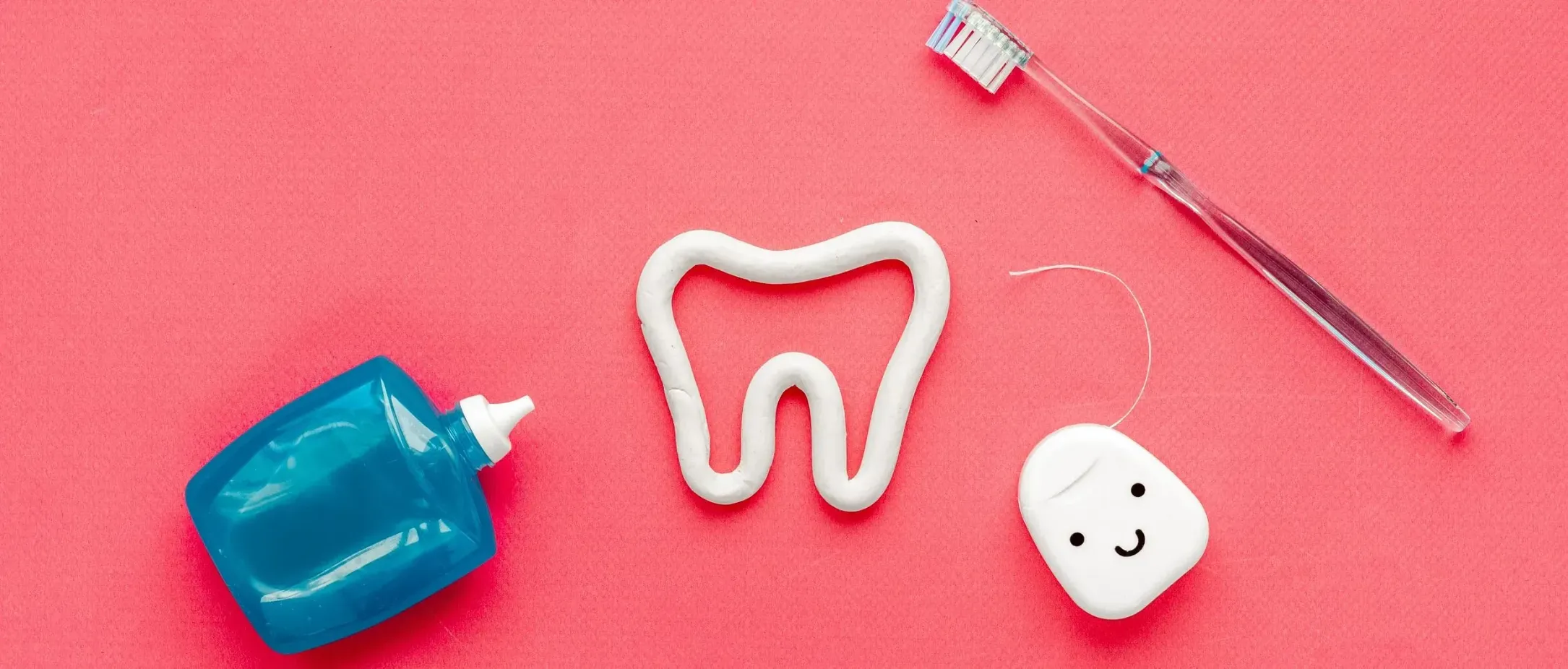Una botella de pasta de dientes, un cepillo de dientes y un hilo dental sobre una superficie rosa.