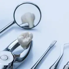 Un diente está colocado encima de un par de alicates al lado de un espejo dental.