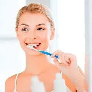 Una mujer se cepilla los dientes frente a un espejo.