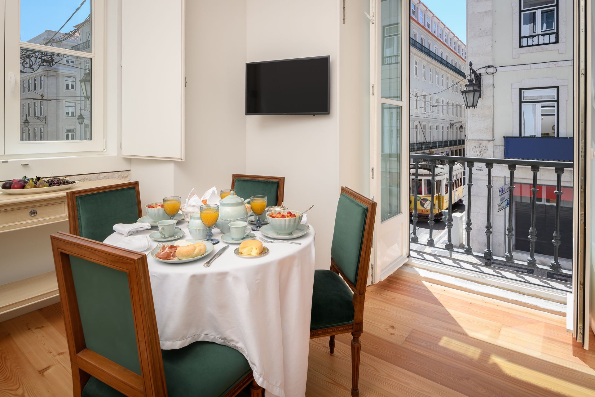 Dining room with a table set for breakfast and a balcony overlooking a city street.