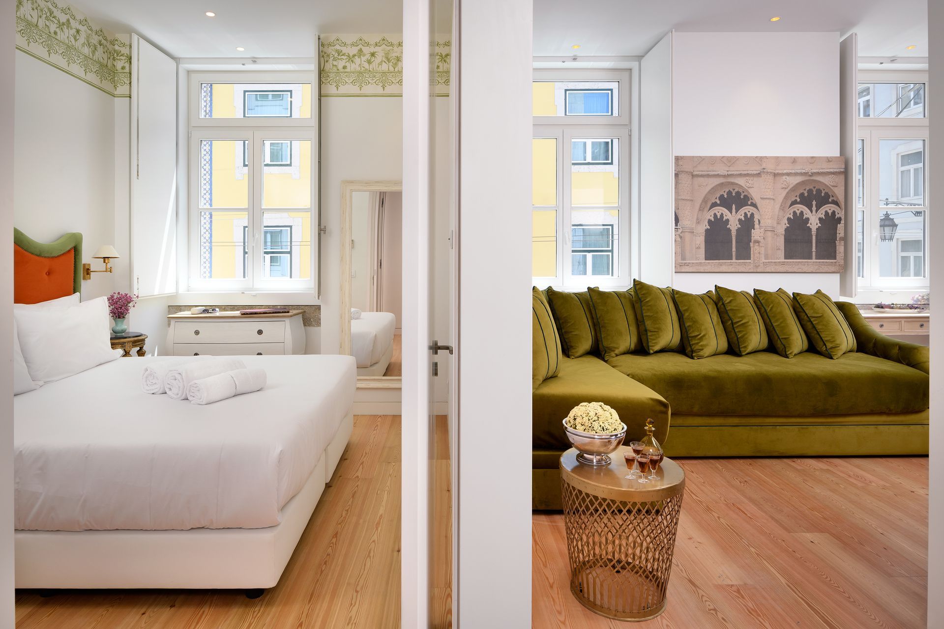 Bedroom and living room with wooden floors, olive green sofa, and white walls.