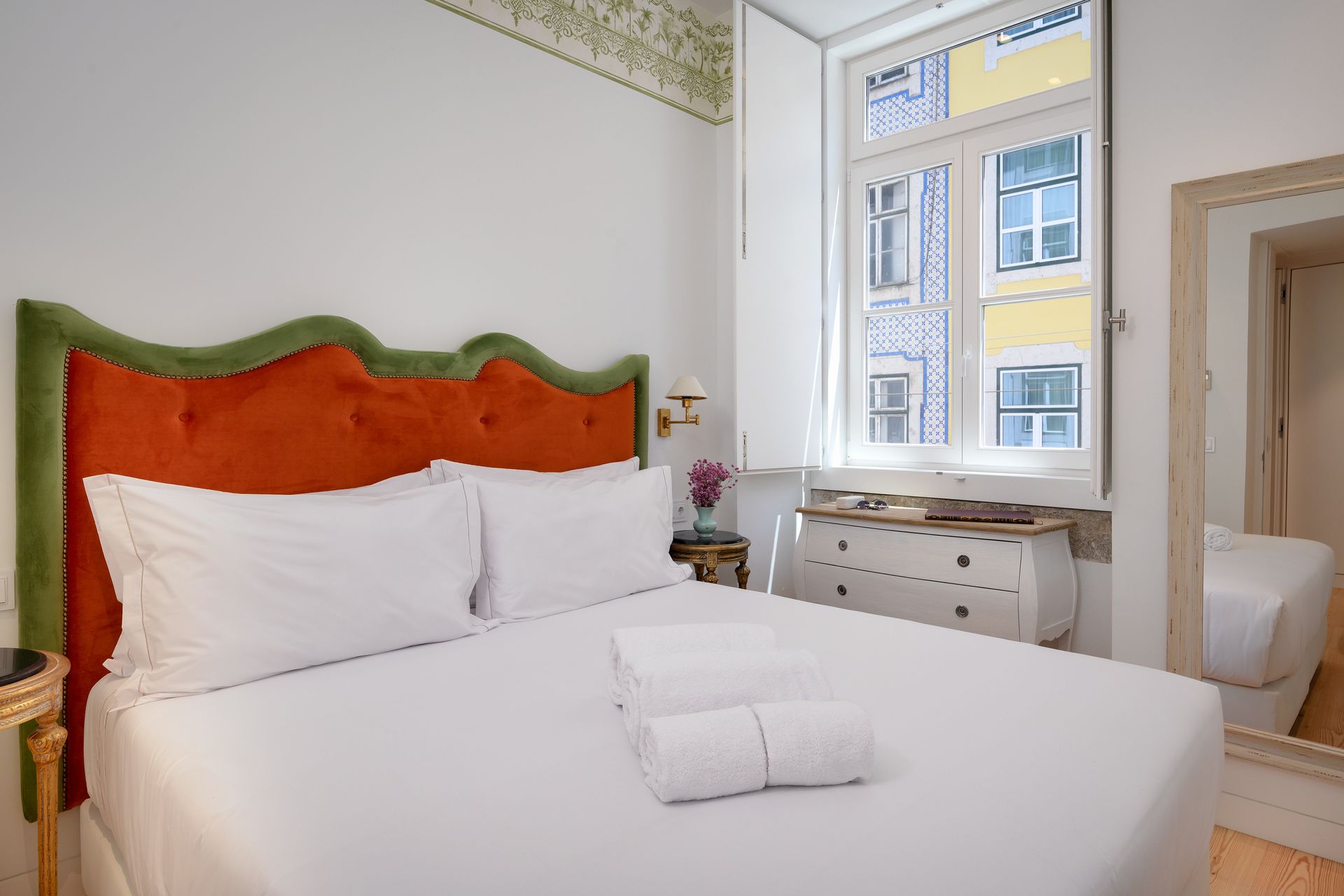 Bedroom with orange headboard, white bedding, window, dresser, and mirror.