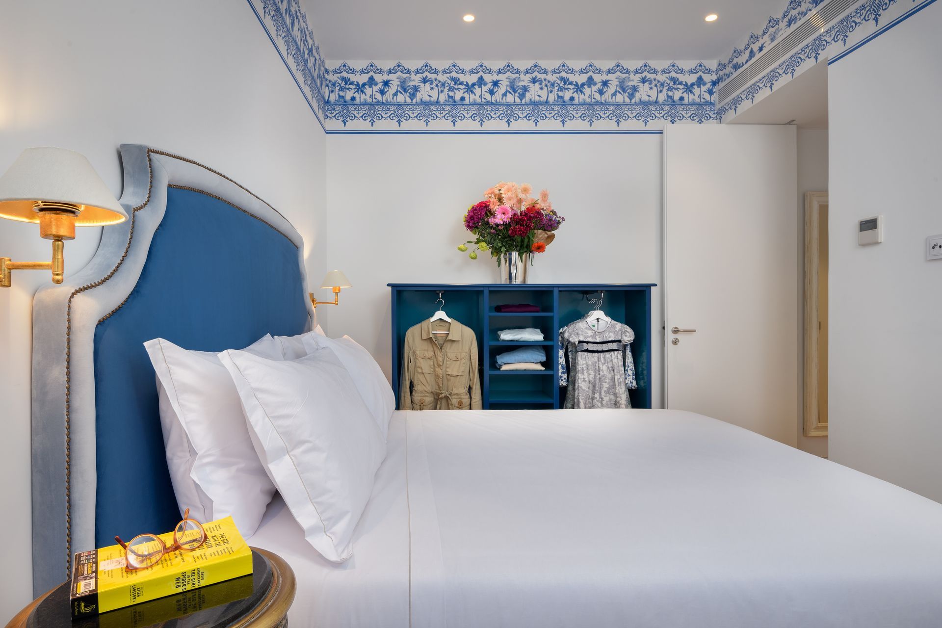 Bedroom with blue headboard, white bedding, open closet, and floral ceiling trim.