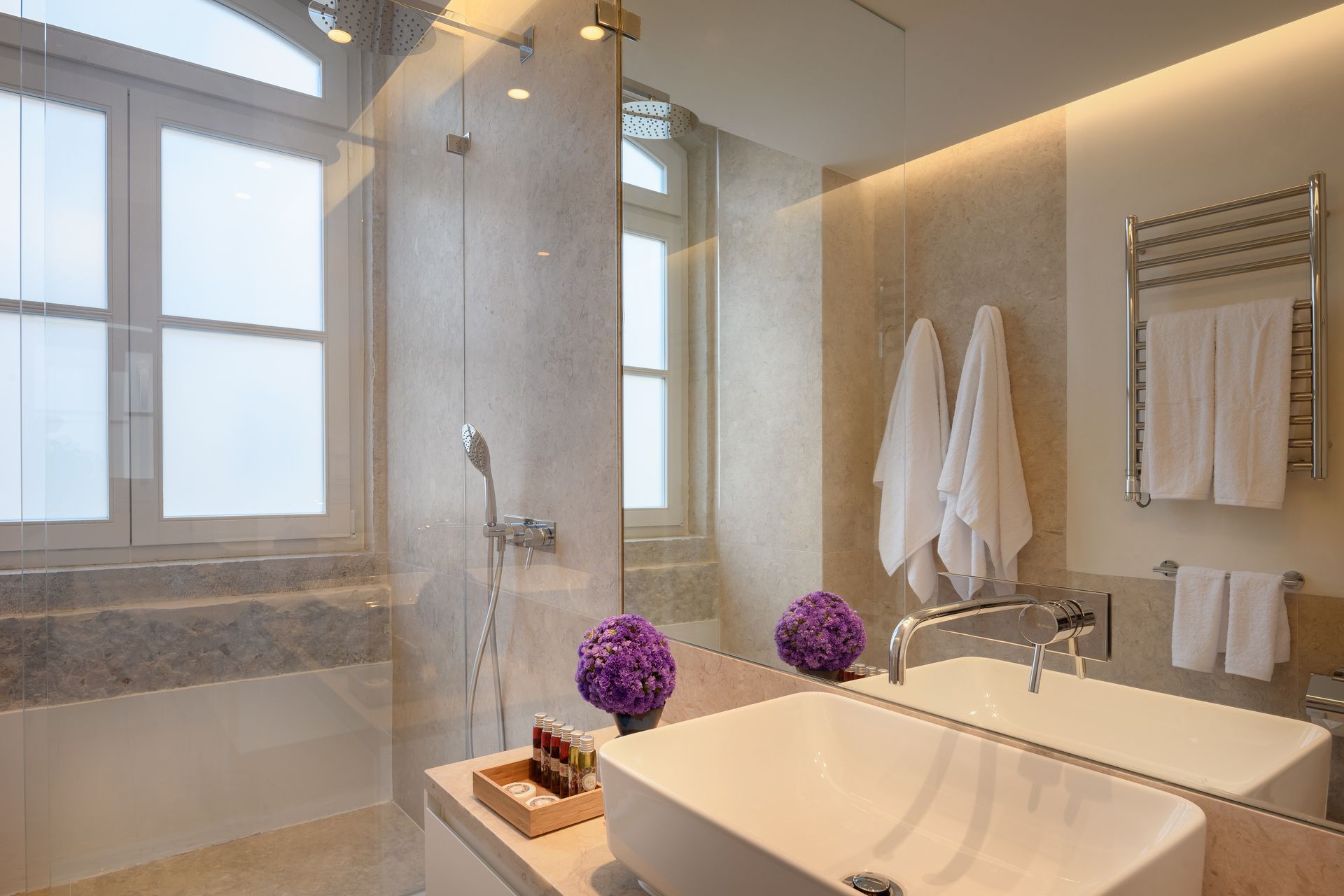 Luxurious bathroom with a white sink, large mirror, and glass shower. Two windows let in light.