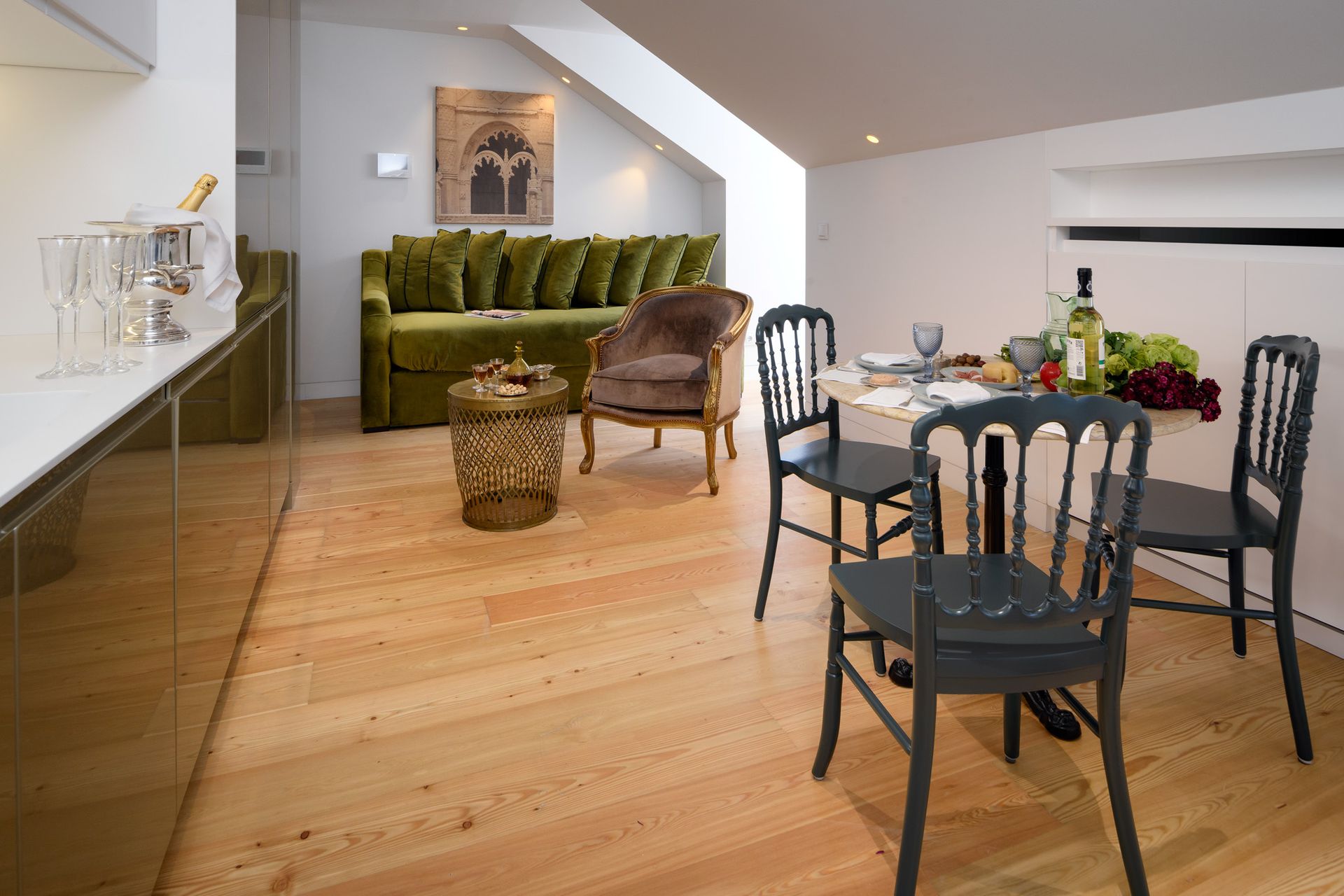 Modern living space with hardwood floor, green sofa, dining table, and kitchen counter.