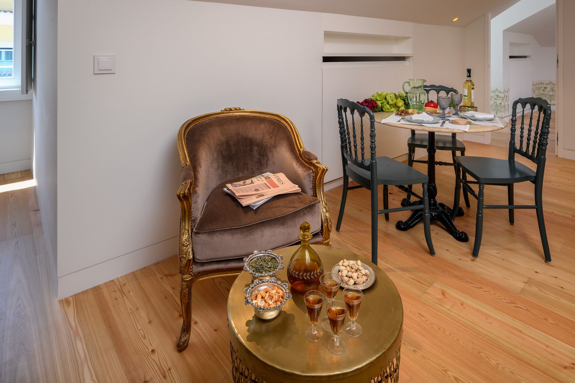 Living space with gold-framed chair, round table, and snacks on a gold table.