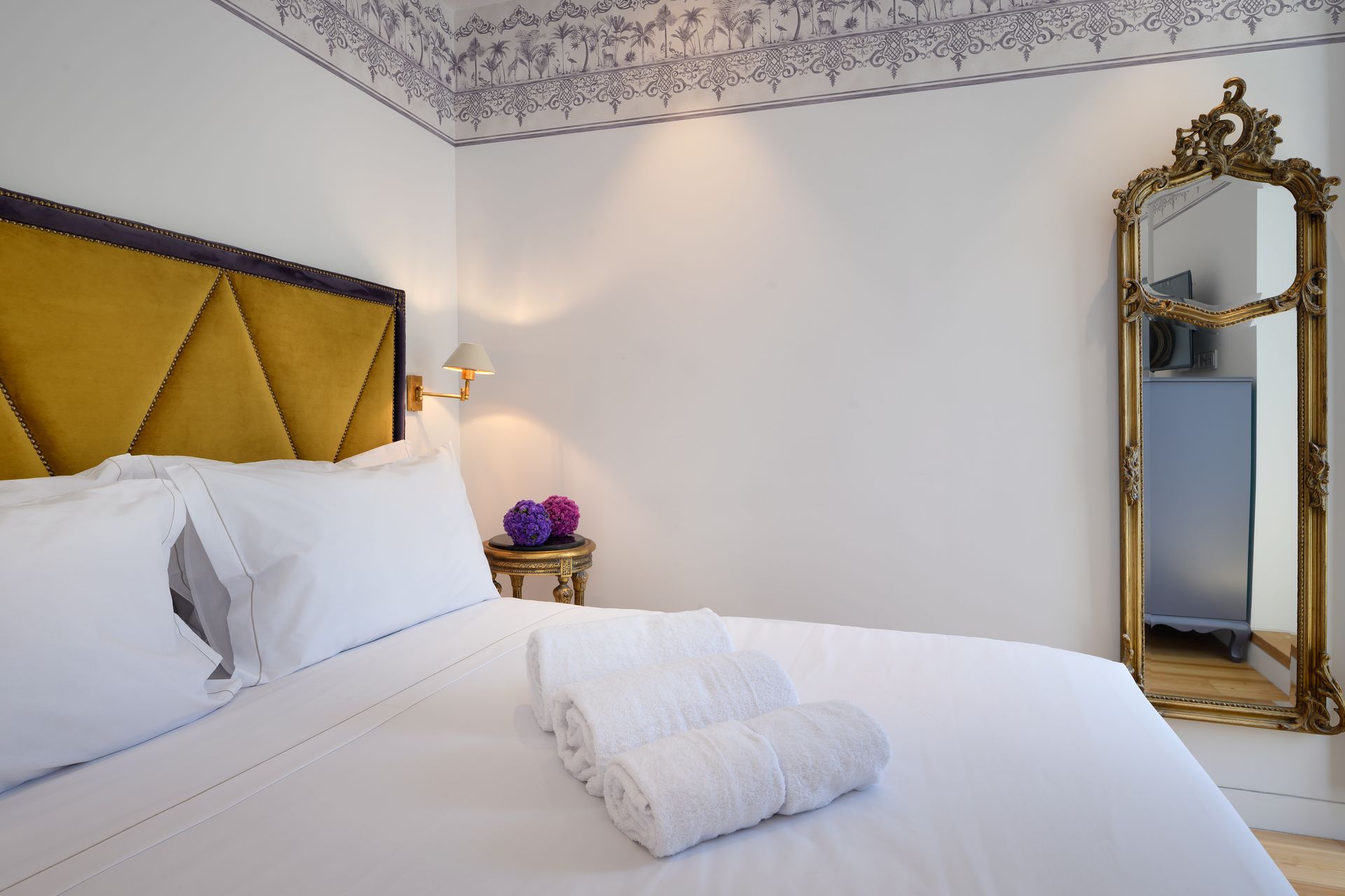 Bedroom with a gold-framed mirror, a yellow headboard, white linens, and decorative ceiling trim.