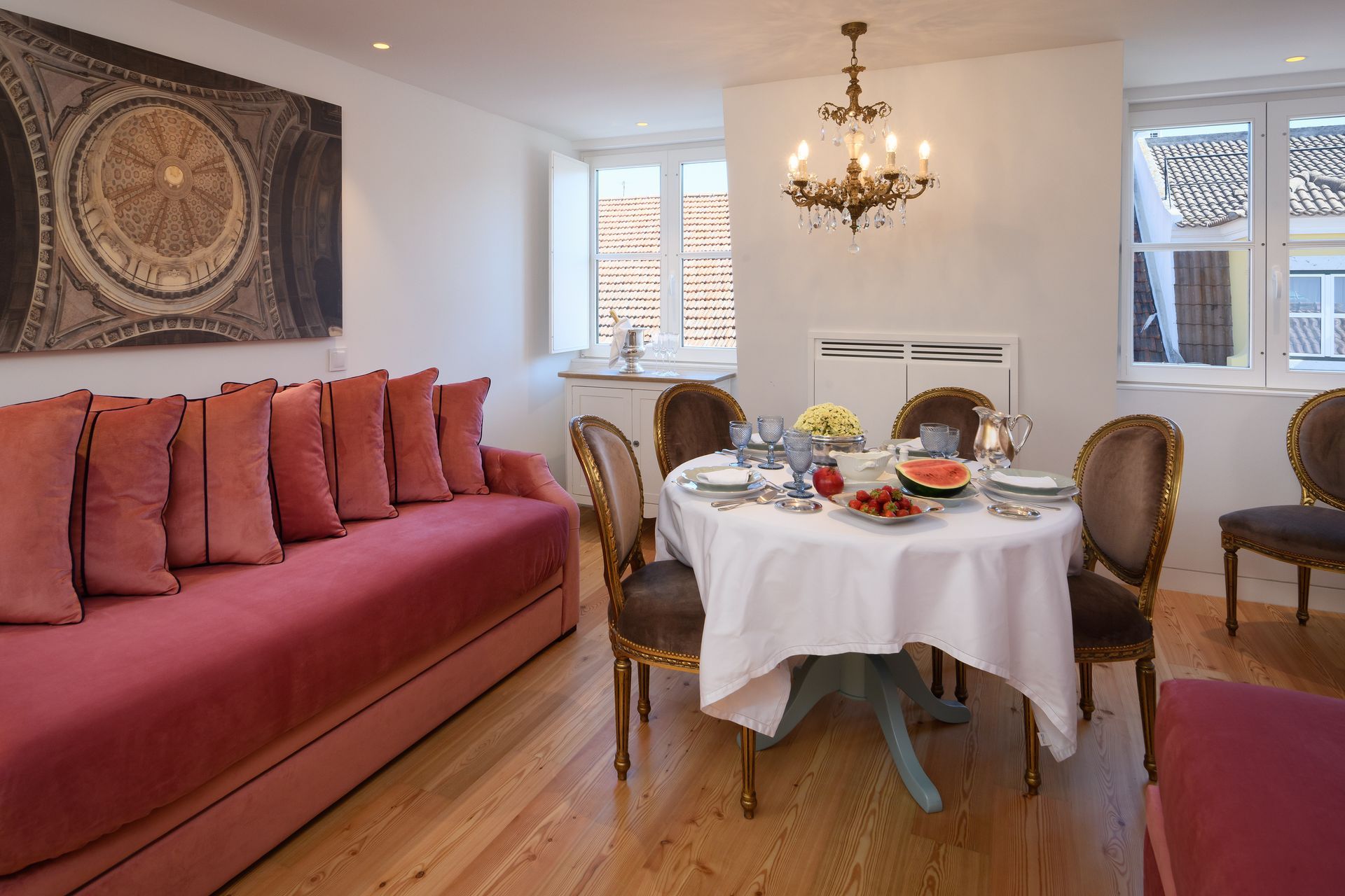 Living room with red sofa, round dining table set with food, chandelier, and artwork.