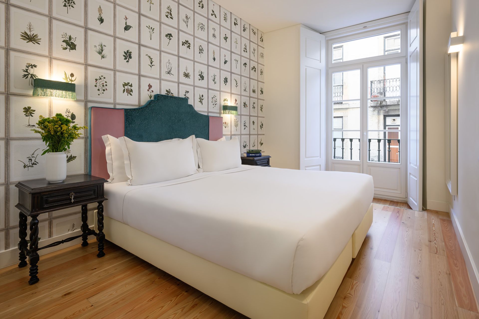 Bedroom with a bed, nightstand, and window overlooking a balcony. Floral print wallpaper.