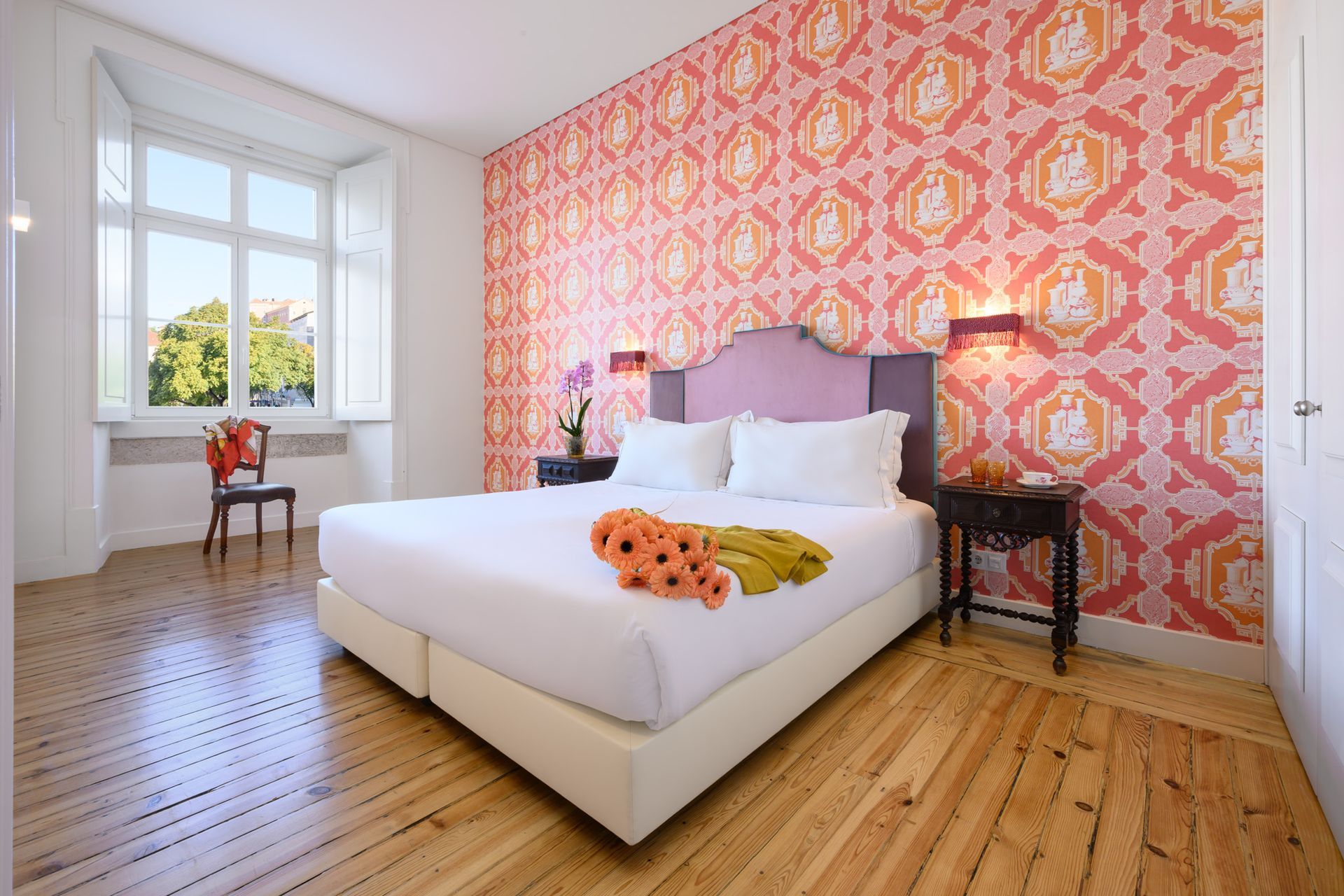 Bedroom with floral patterned wall, bed, window, and wood floor.