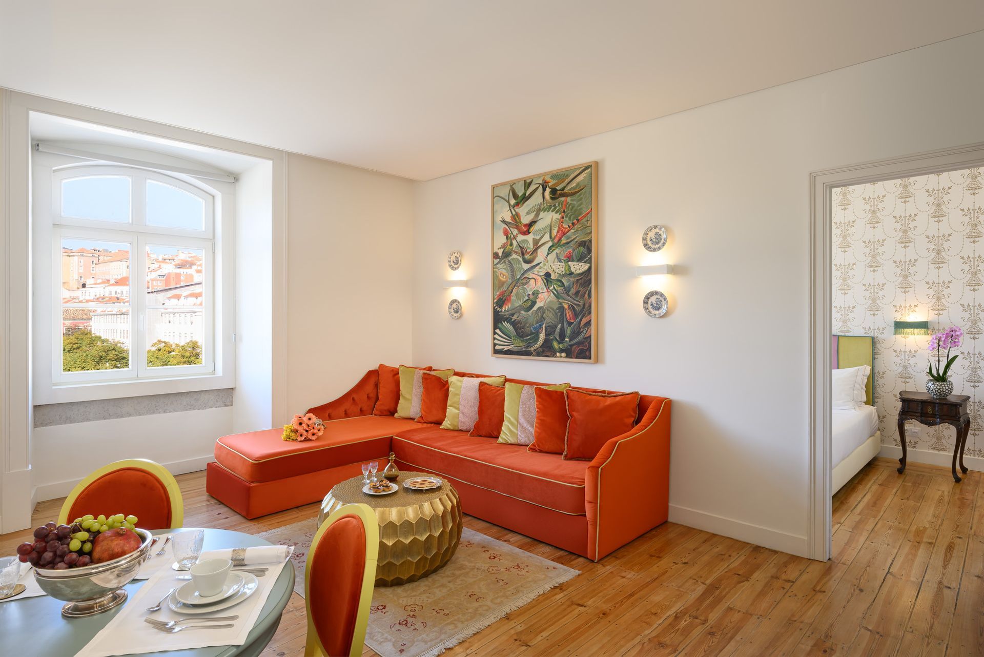 Bright orange sofa in living room with view, art, and open doorway to bedroom.