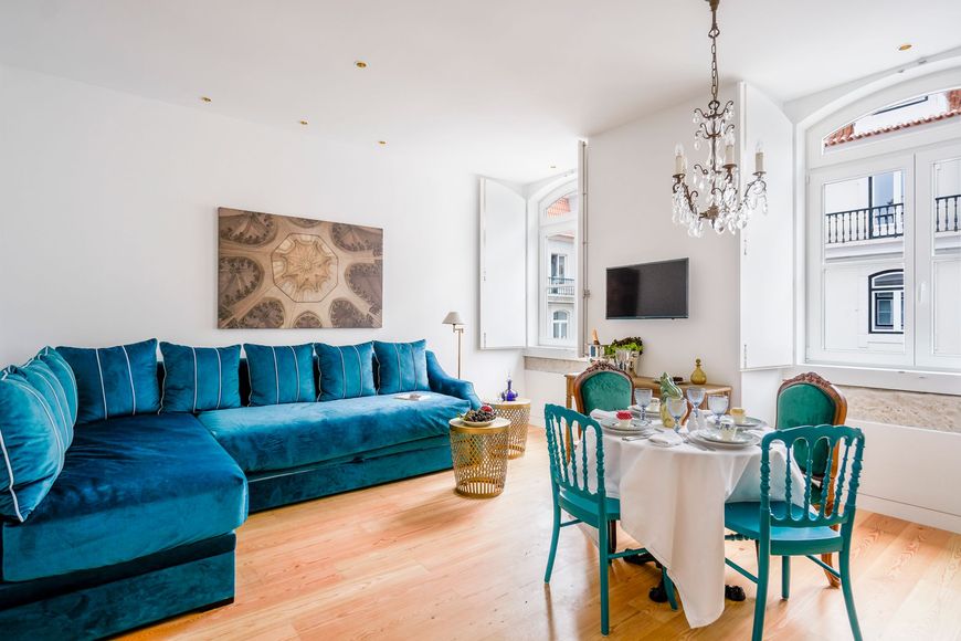 Living room with teal sofa and dining set, chandelier, and large windows.