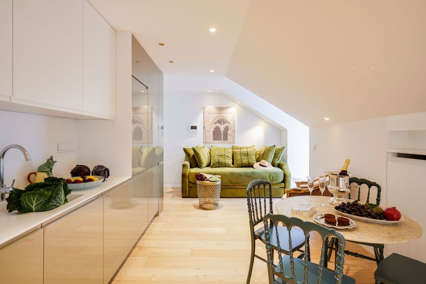 Modern, bright apartment with kitchen, dining area, and green sofa under a sloped ceiling.