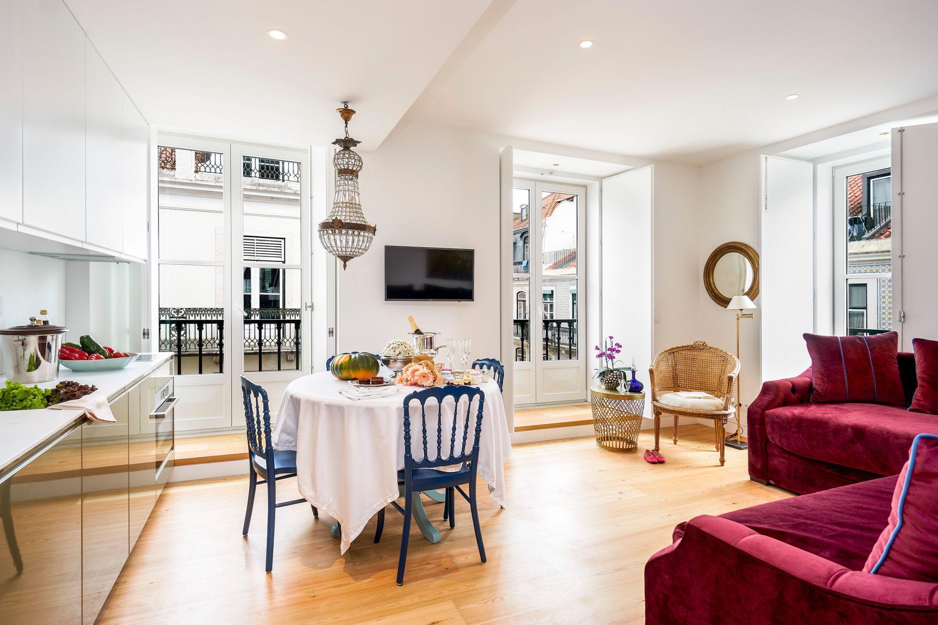 Bright living space with kitchen, dining area, and red sofa, with a chandelier and windows overlooking a balcony.