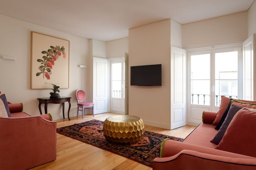 Living room with pink sofas, antique table, ornate rug, and large botanical print.
