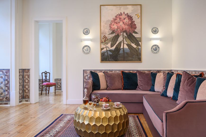 Living room with mauve sofa, gold coffee table, botanical art, and tiled wall.