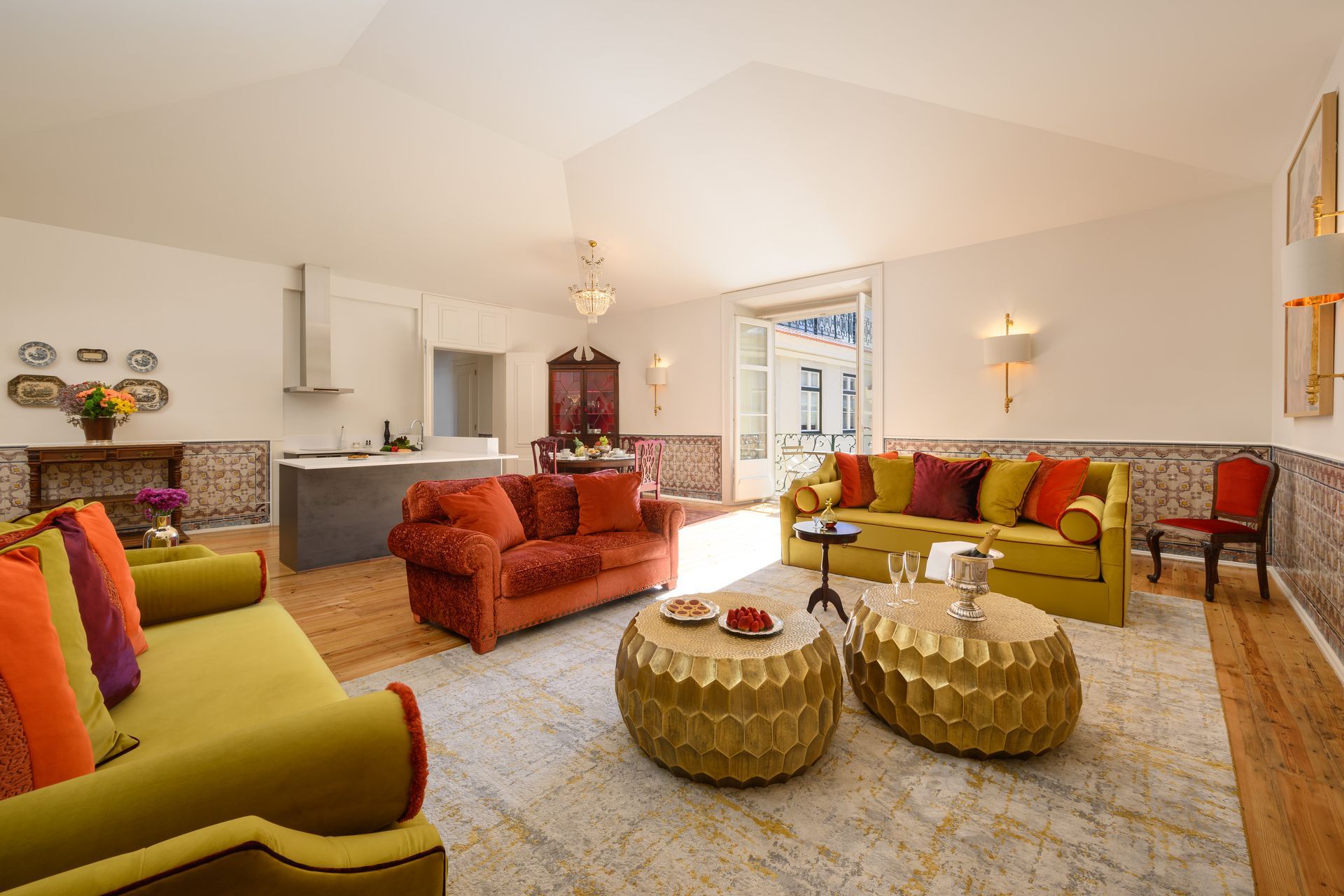 Living room with colorful couches, golden tables, and patterned tile. Sunlight streams in.