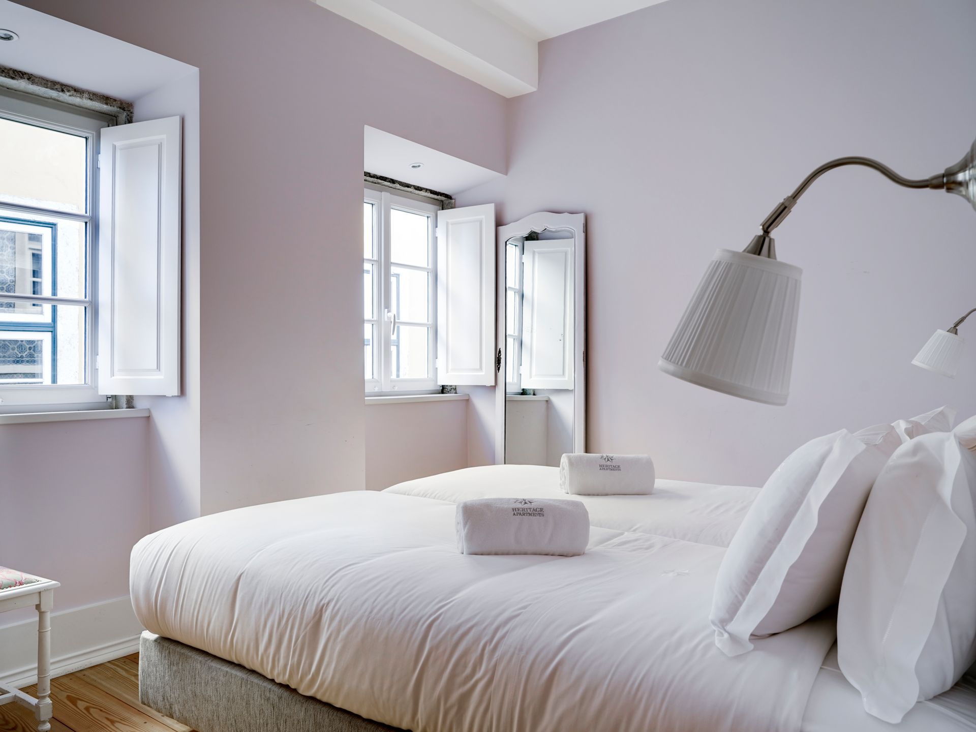 Soft pink bedroom with white bedding and large windows in a spa deluxe two-bedroom apartment.