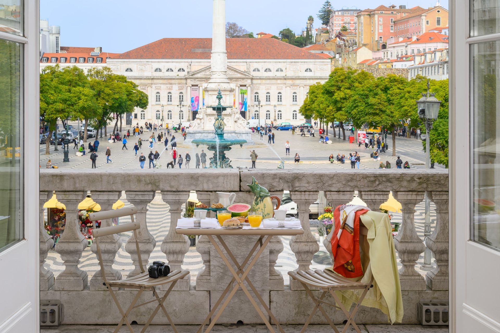 Balcony overlooking Lisbon square with people, breakfast table, and ornate railing.