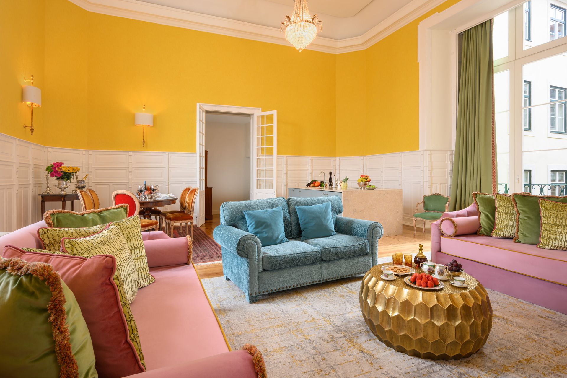 Living room with yellow walls, colorful couches, and a gold coffee table.