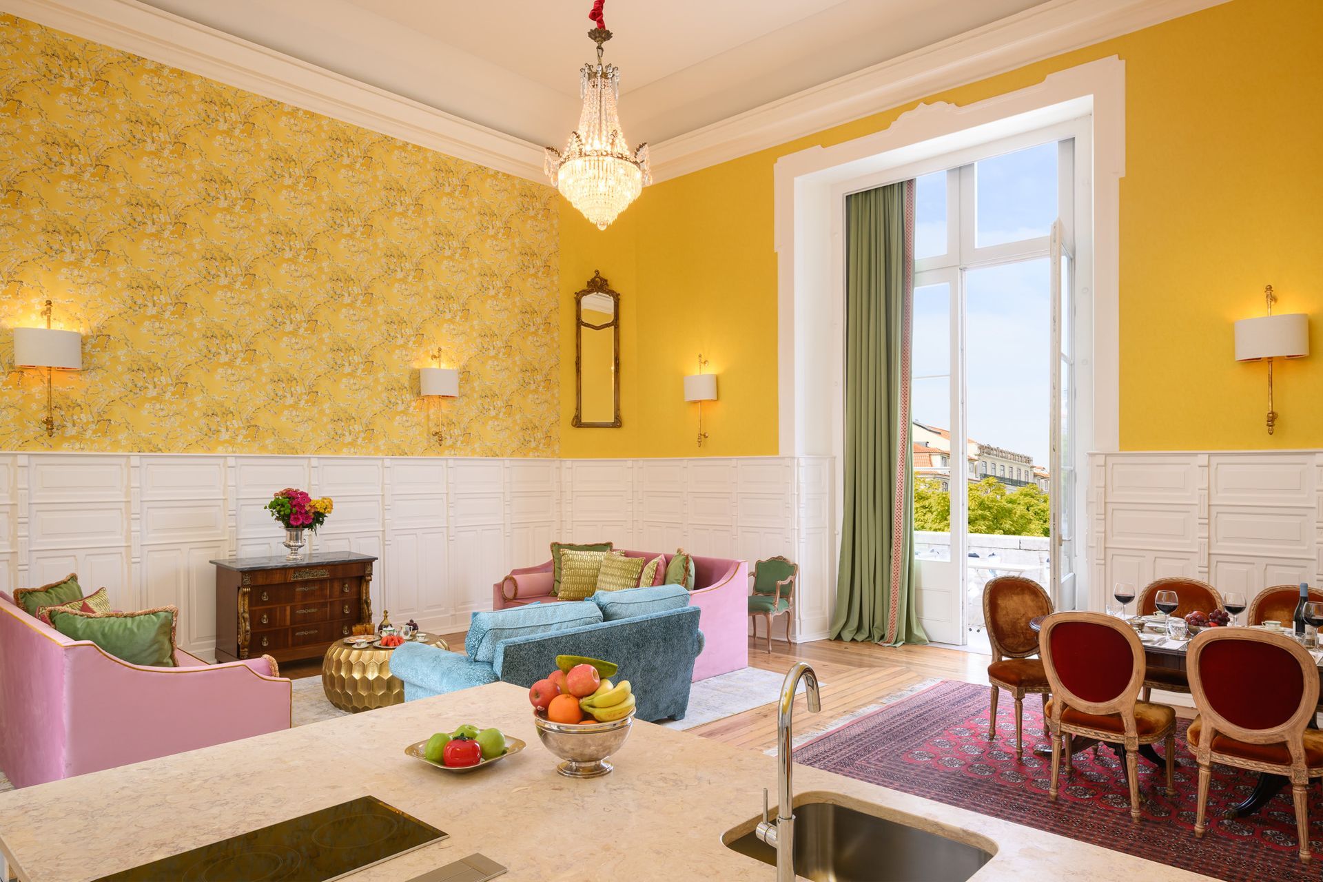 Yellow living room with a pink sofa, blue couch, dining table, and large window.