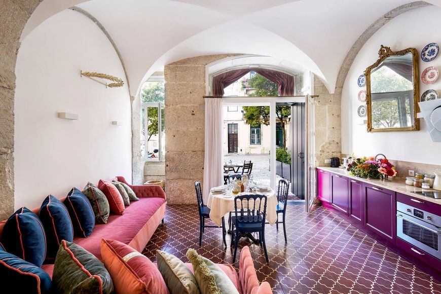 Living room with arched ceiling, pink sofa with blue pillows, purple cabinets, and open doors to patio.