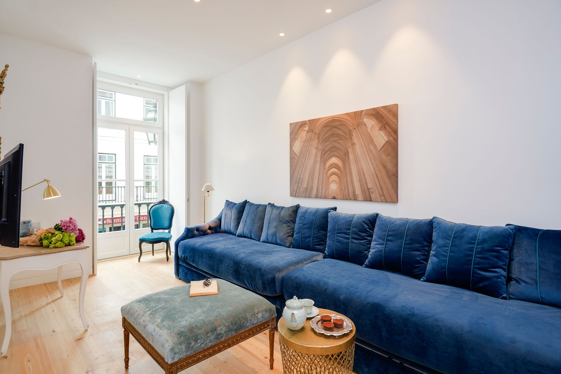 Living room with blue velvet sectional sofa, small ottoman, and gold side table.