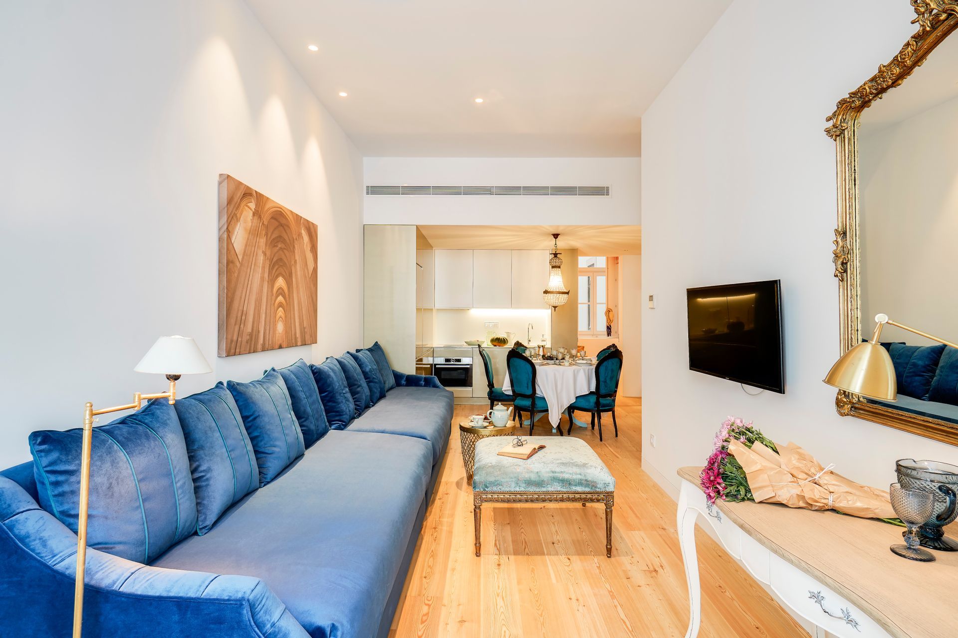 Living room with blue sofa, gold mirror, dining table in the background, hardwood floor.