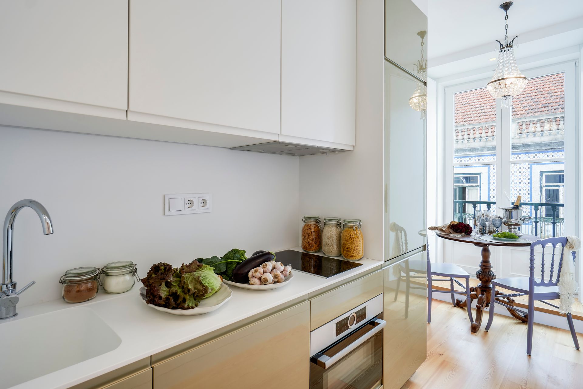 Modern kitchen with fresh vegetables, stainless steel sink, and small dining table by a window.